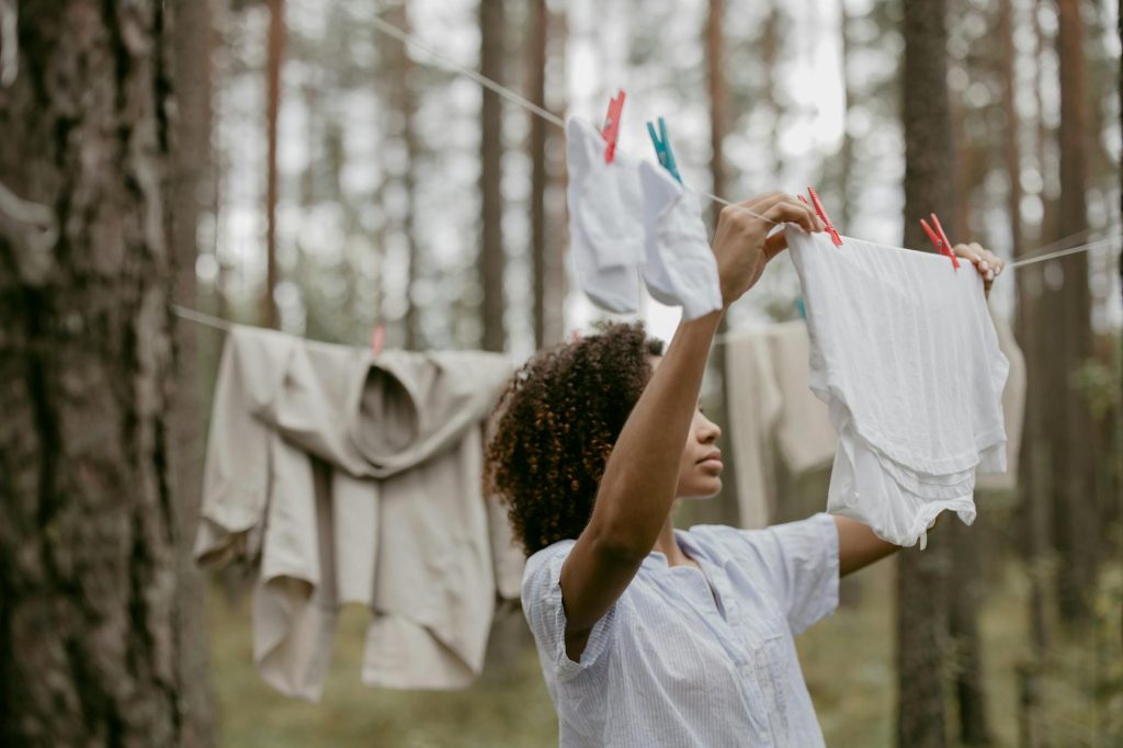 An African woman hangs laundry on a clothesline surrounded by a serene forest, blending nature and daily life.