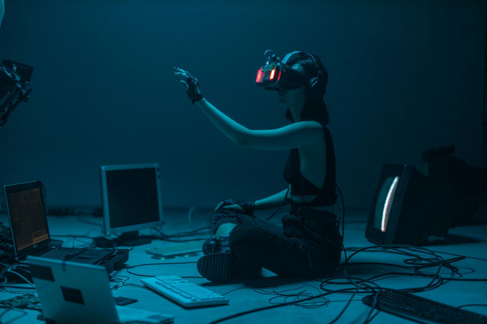 Woman immersed in virtual reality, surrounded by tech, in a dimly lit room.