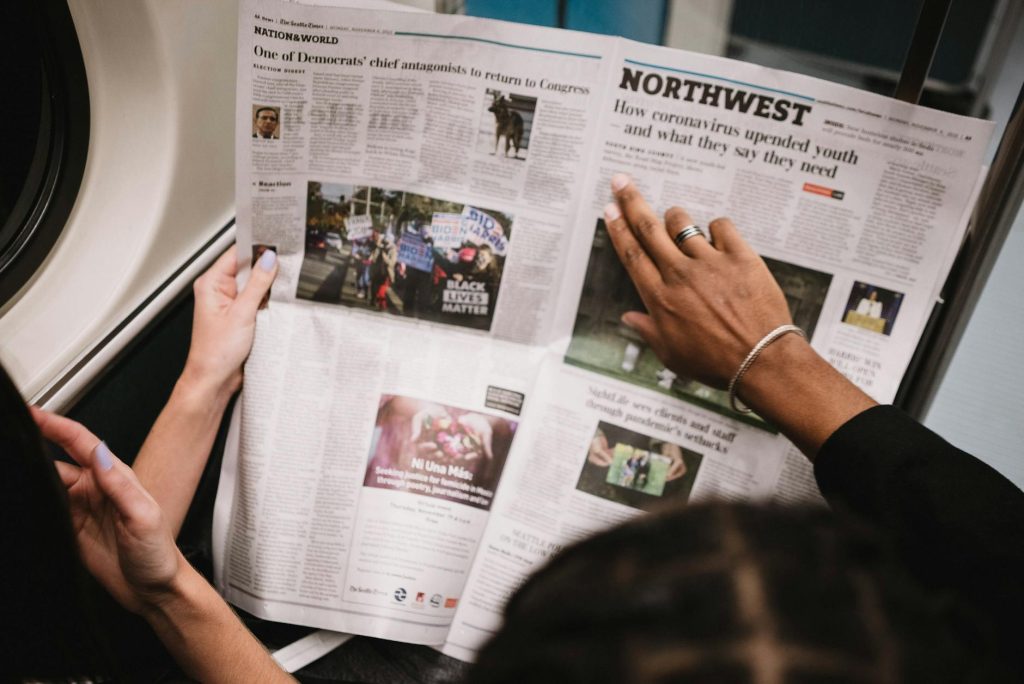 People reading a newspaper on a subway train, highlighting current events and diverse perspectives.