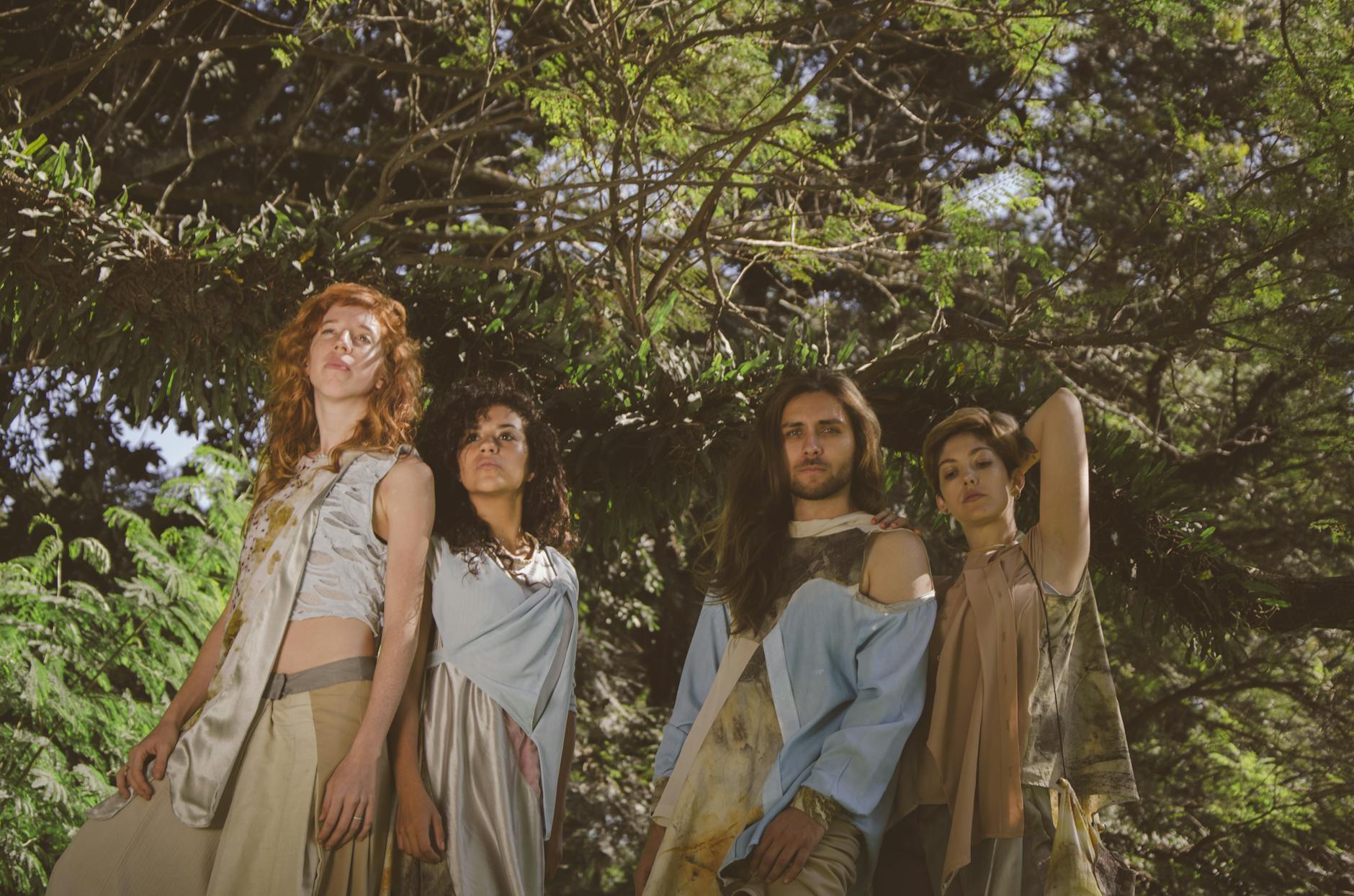 A group of diverse models posing in stylish recycled outfits under lush forest canopy.