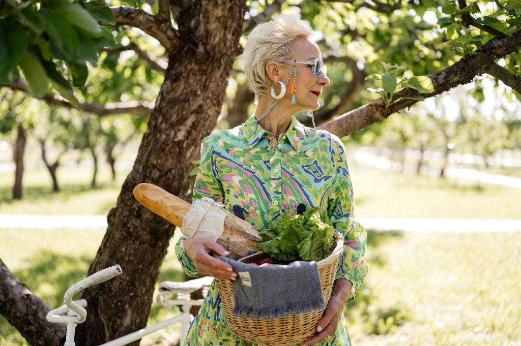 A fashionable senior woman holding a picnic basket in a sunny park, exuding style and elegance.