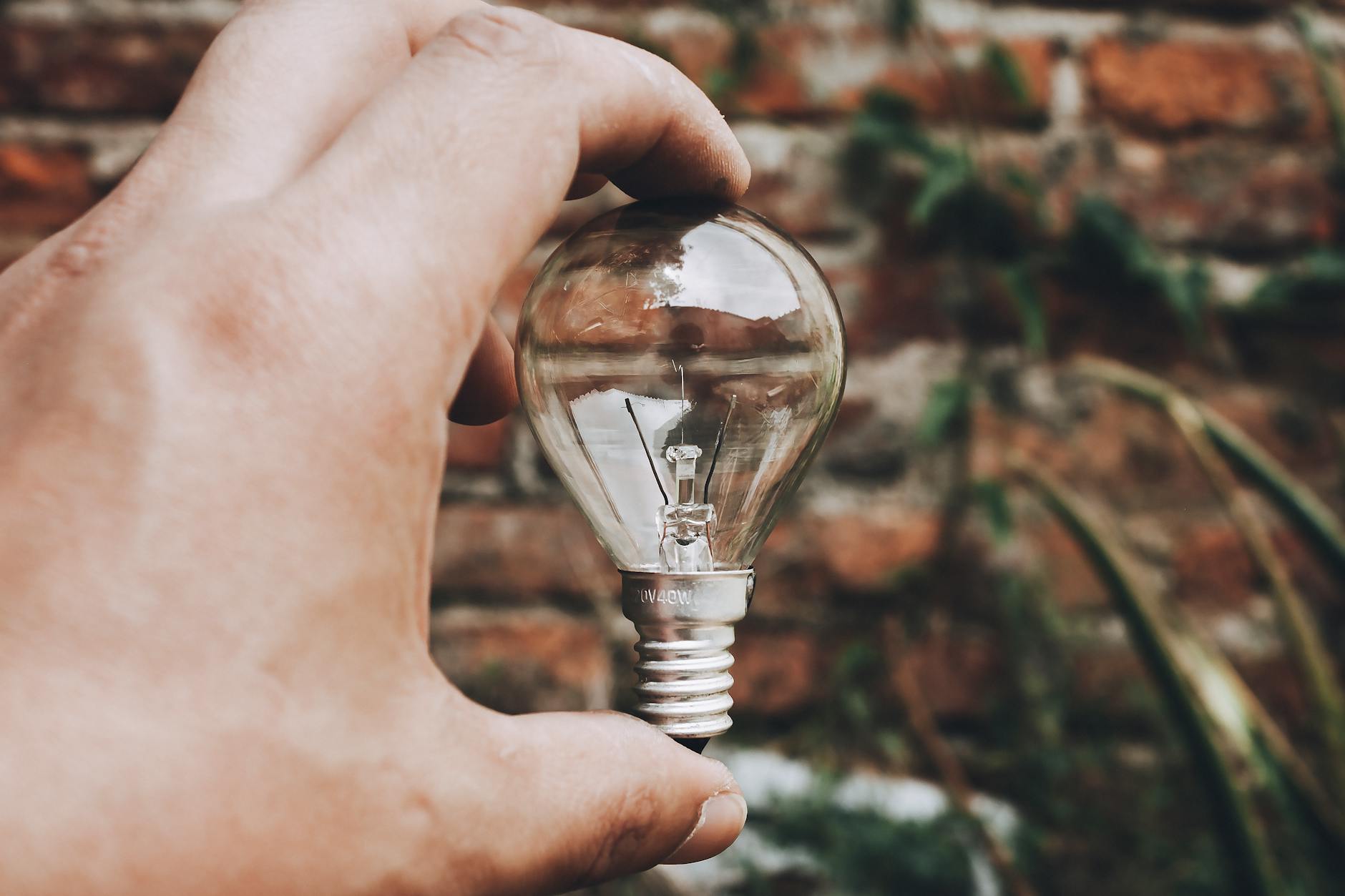 Close-up of hand holding a clear light bulb with a brick wall background, capturing innovative and eco-friendly themes.