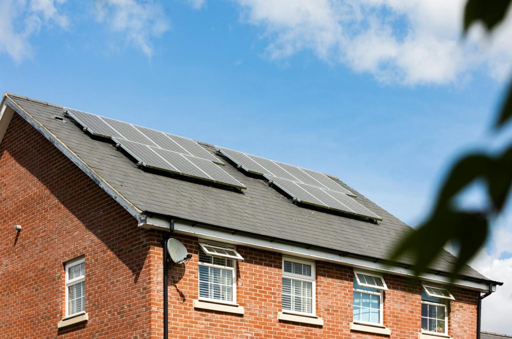 Brick house featuring solar panels on the roof under a clear blue sky, promoting sustainable energy.
