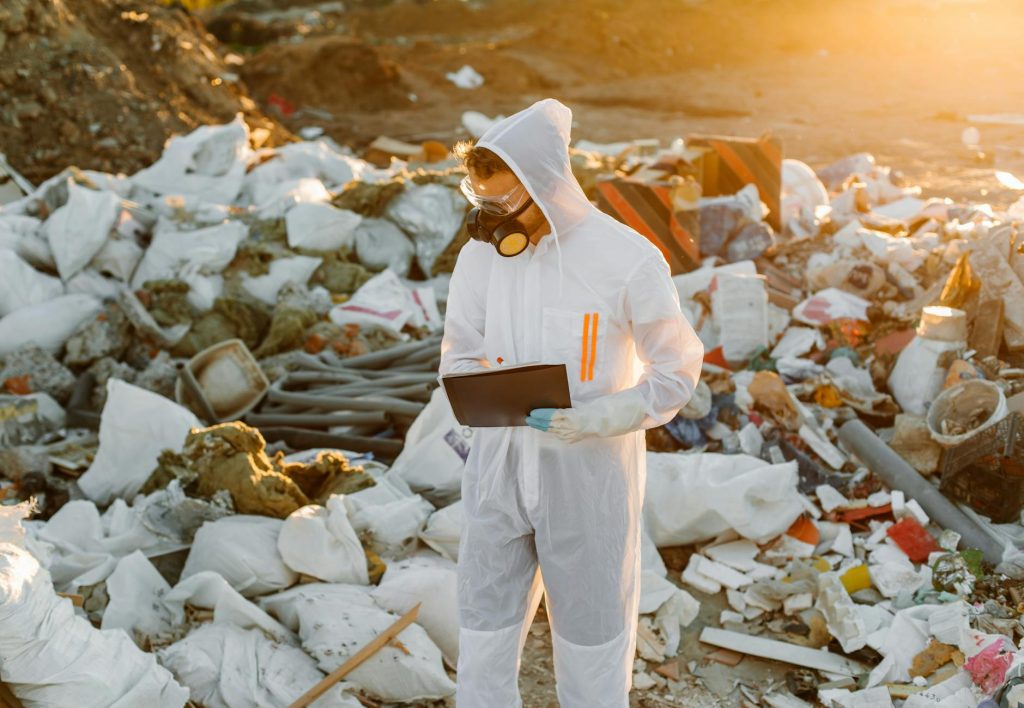 An environmental scientist in protective gear surveys a landfill for research and pollution control.