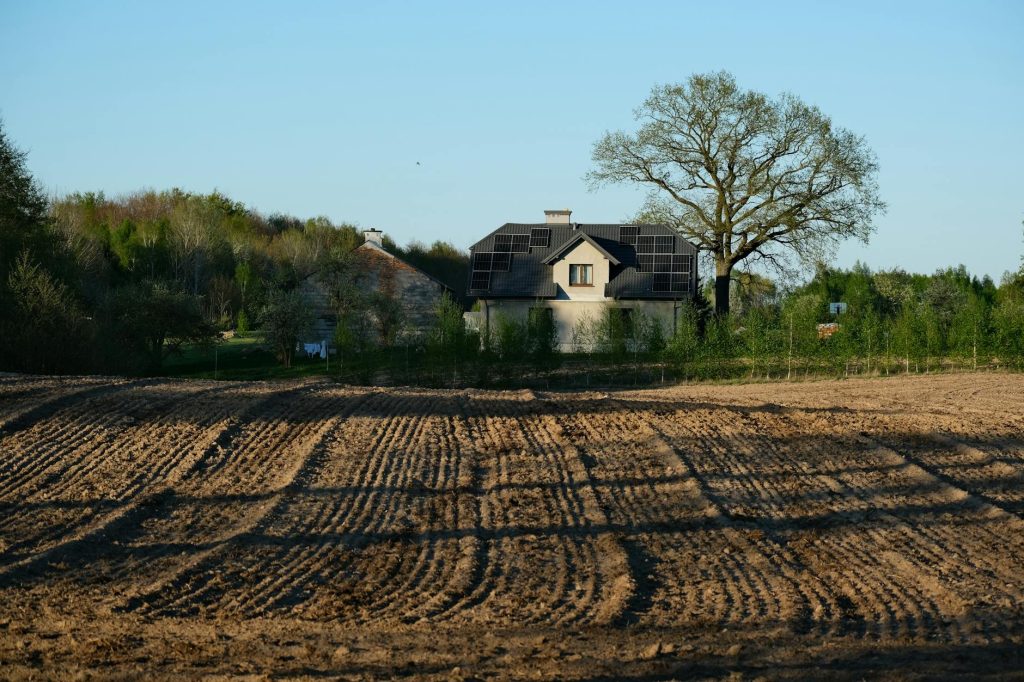 Modern house with solar panels surrounded by field and trees on a clear spring day.