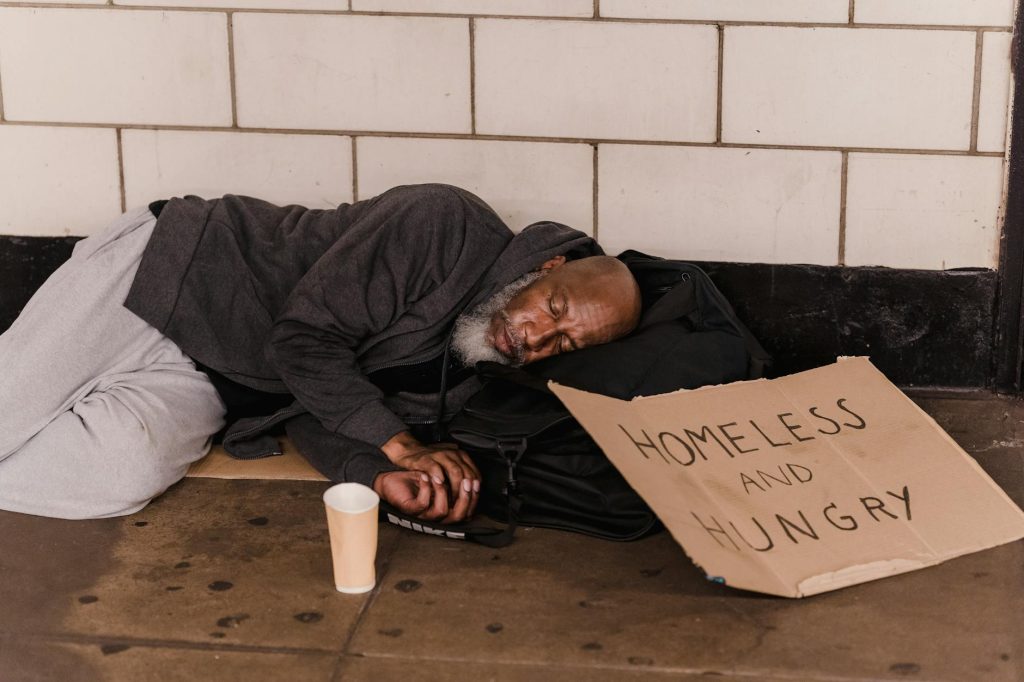 A homeless man sleeping on the street with a cardboard sign, capturing urban hardship.