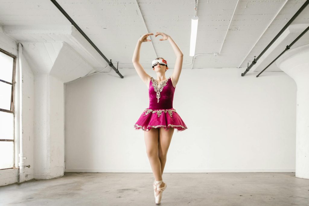 Ballerina in pink costume using virtual reality headset indoors. Futuristic dance concept.