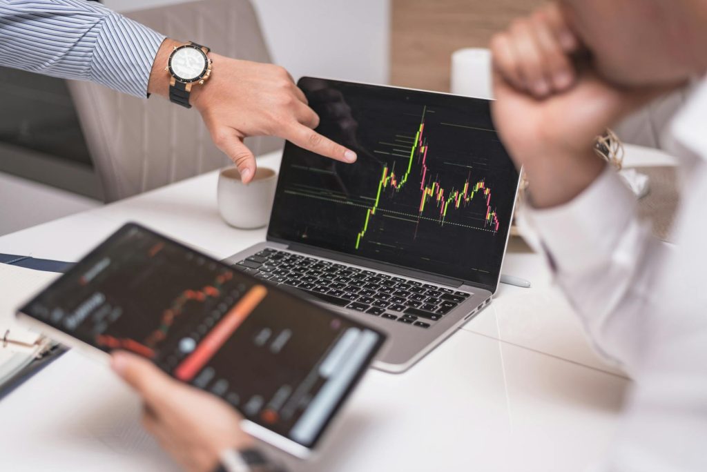 Business professionals analyzing cryptocurrency market trends on laptop and tablet.