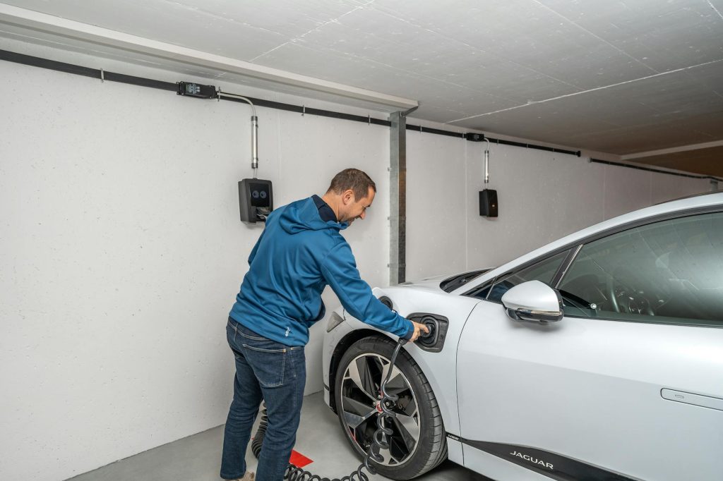 A man connects an electric car to a charging station in a modern indoor garage setting.