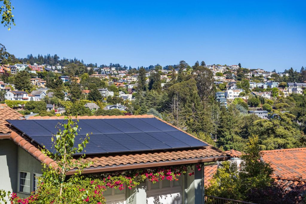 Solar panels on a suburban home, surrounded by lush greenery and a sunny blue sky.